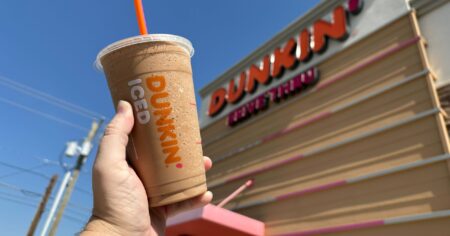 hand holding an iced coffee in front of a Dunkin building