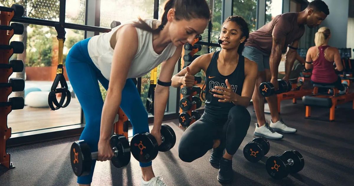 Orange Theory coach talking to a woman lifting weights