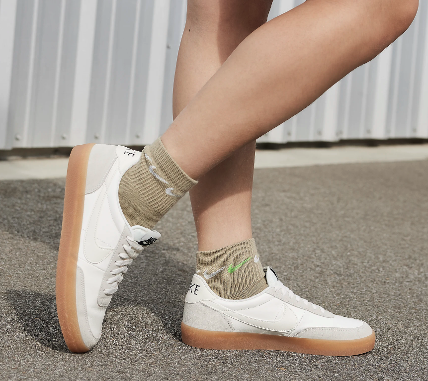 Women in brown socks wearing gray and white Nike Killshot shoes