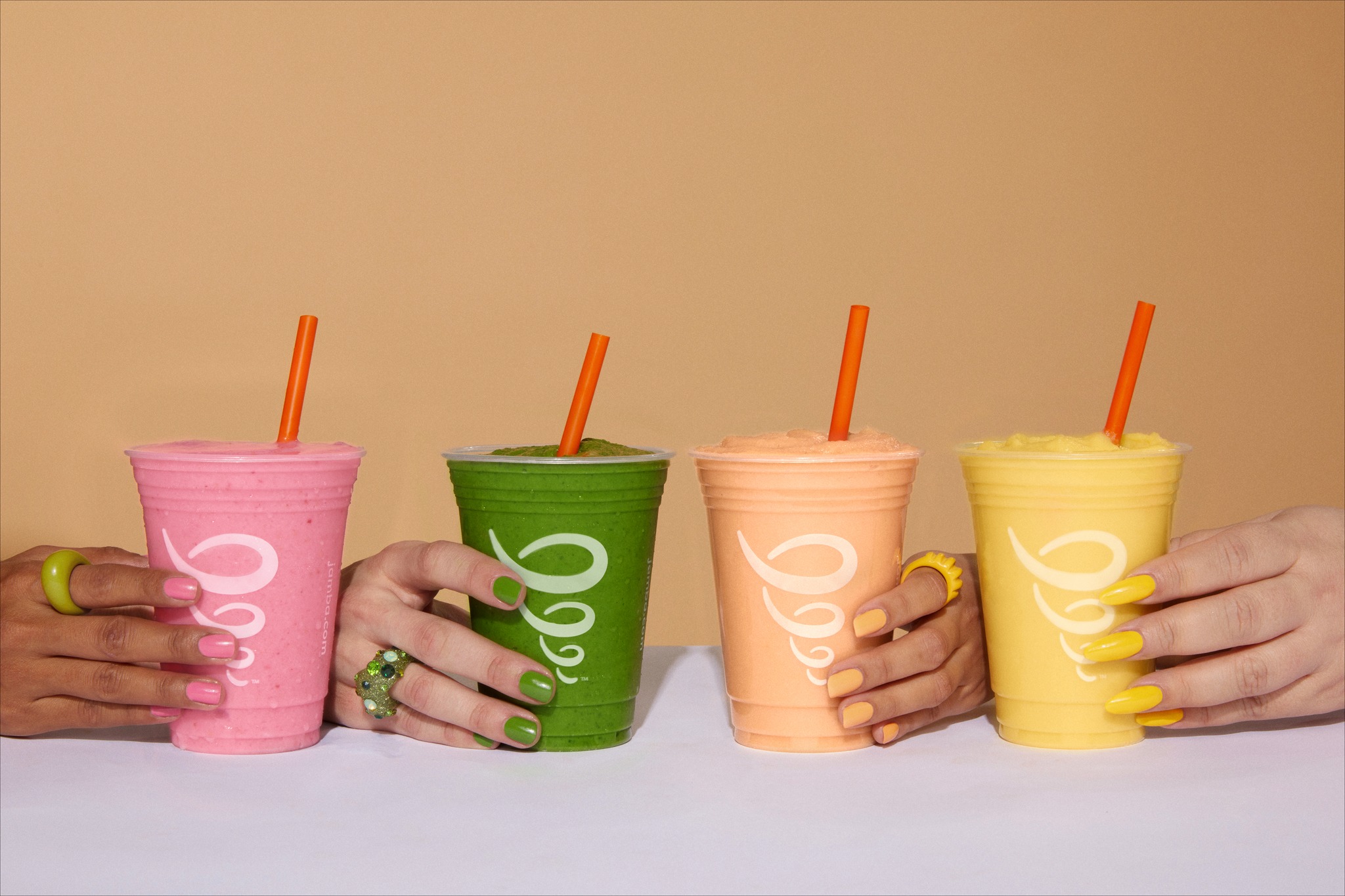 hands on a table each holding a different flavor of jamba juice smoothie free jamba juice