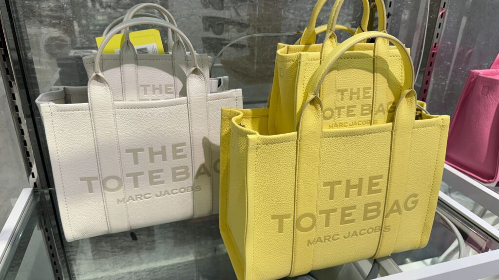white and yellow marc jacobs the tote bags sitting on a shelf