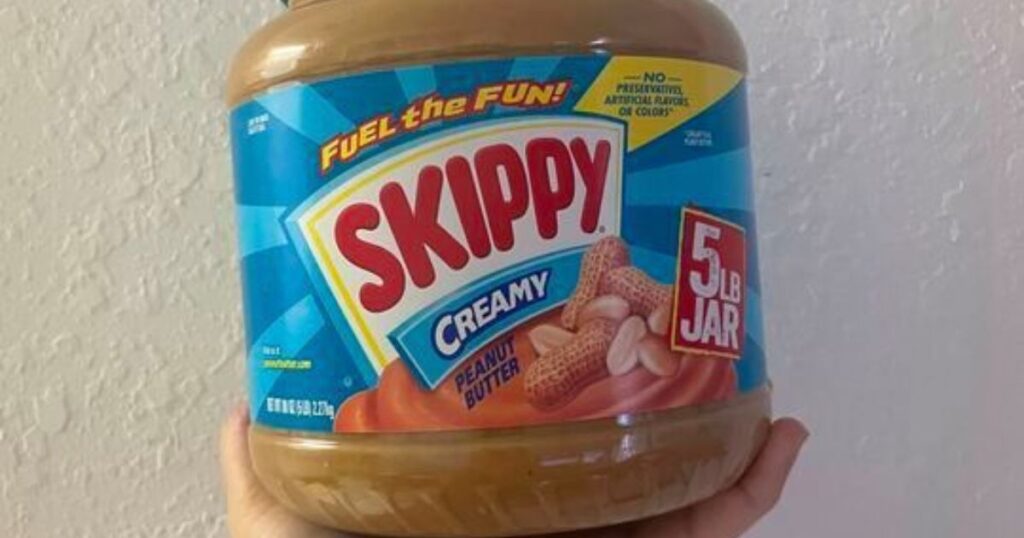 hand holding a big jar of peanut butter