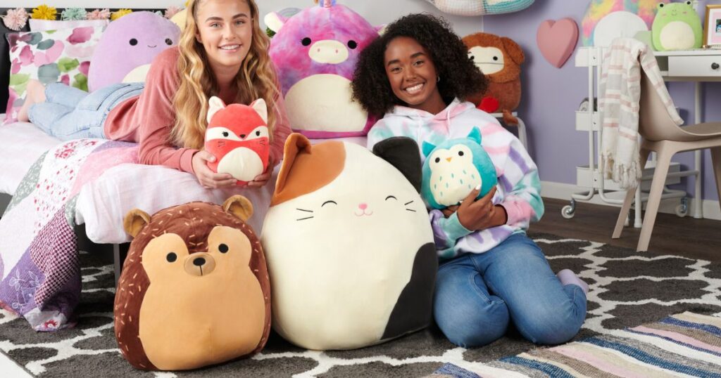 girls sitting by a bed holding Squishmallows
