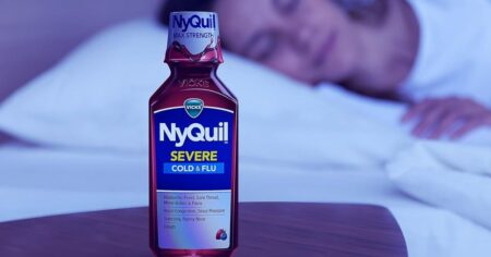 bottle of Nyquil on a nightstand with a woman sleeping in the background