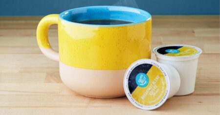 Happy Belly coffee pods next to a mug of coffee