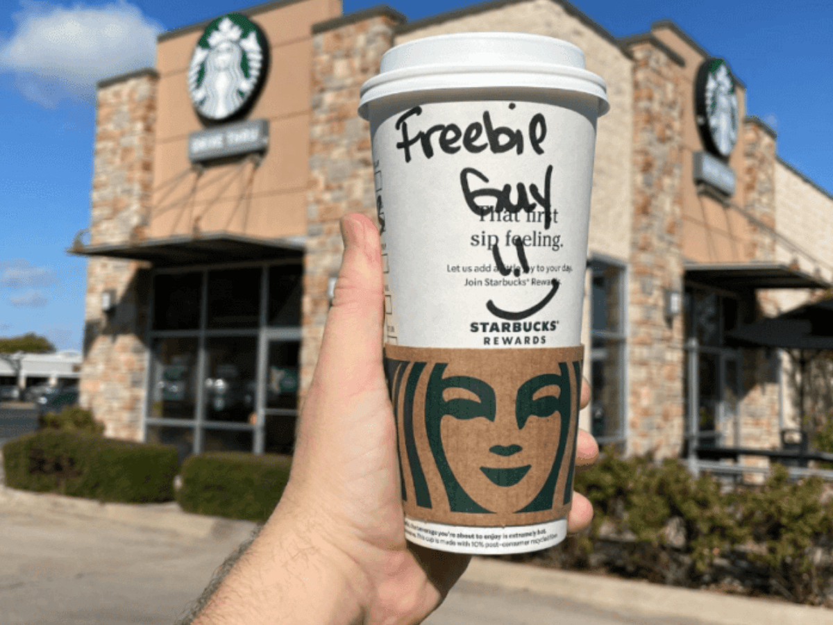 Hand holding up Starbucks drink in front of coffee house